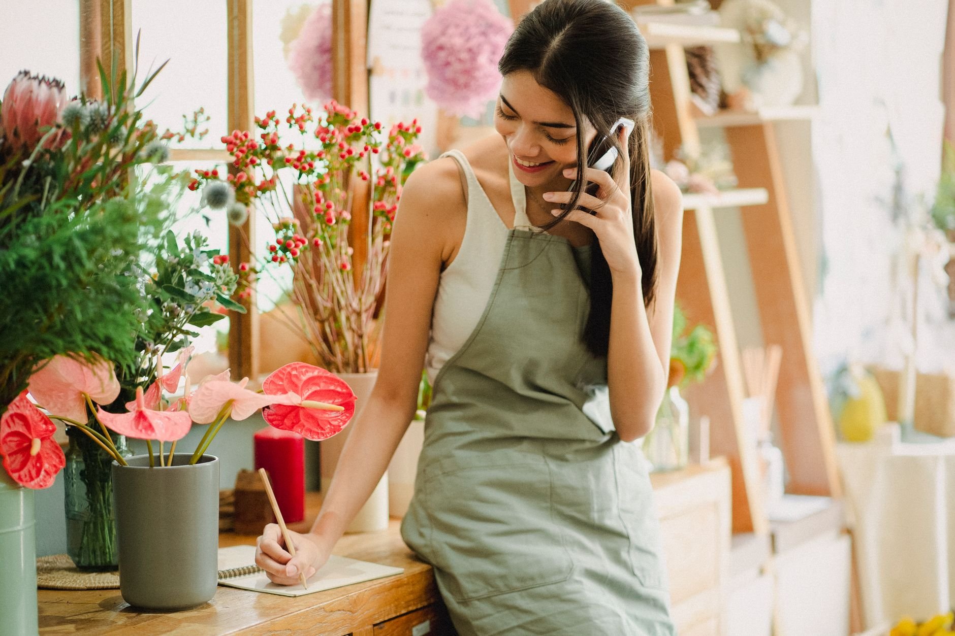 Smiling small business owner talking on mobile phone while working in her shop
